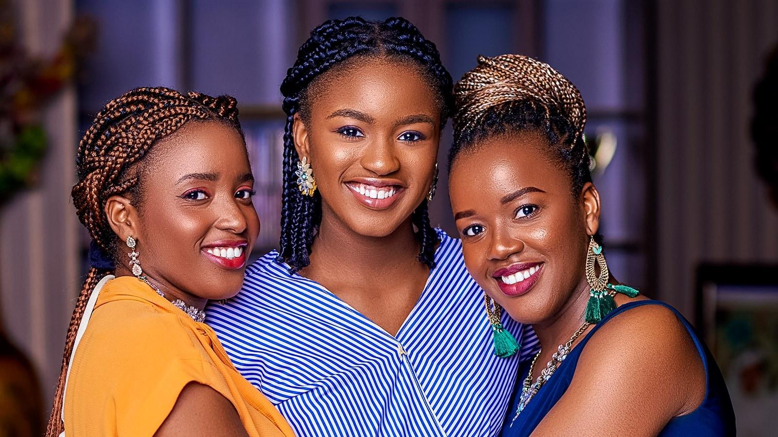 Three sisters, Jemima, Jeiel, and Jesimiel Damina, holding each other closely while posing with bright smiles.